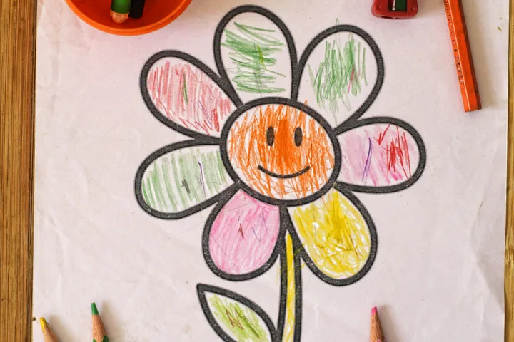 A child's colourful drawing of a smiling flower on paper